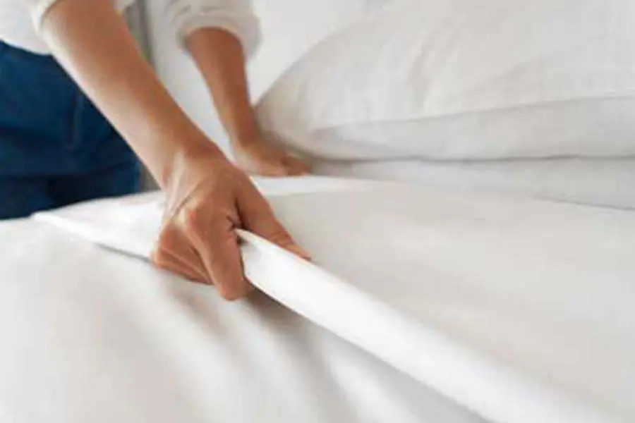 Hands making the bed with white sheets