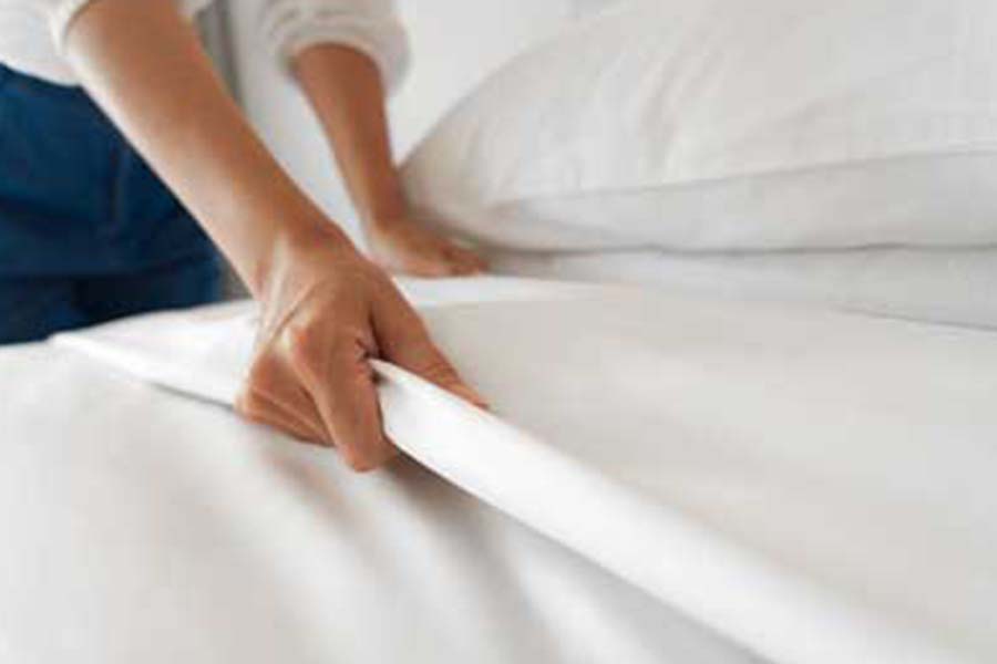Hands making the bed with white sheets