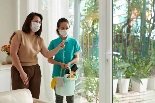 Two people in a home wearing face masks with cleaning supplies